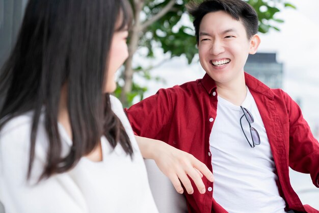 Felicidad alegre pareja asiática joven contacto visual masculino y femenino risa sonrisa juntos diversión conversación relajarse vestido casual encuesta y jardín vacaciones fin de semana resort fondo