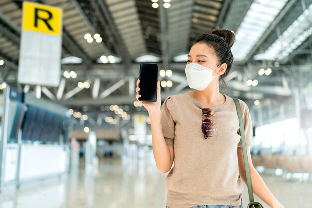 Felicidad asiática mujer viajera mano sostener pantalla de visualización de teléfono inteligente y pasaporte listo para viajar al extranjero en la salida de la terminal del aeropuerto nuevo estilo de vida normal viajar después de que termine el bloqueo de covid