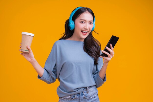 Felicidad despreocupada mujer asiática mujer adolescente usando auriculares mano sostener taza de café escuchar bailar alegre diversión momento en movimiento adolescente usar casaul tela cantando movimiento mientras ríe sonrisa estilo de vida moderno