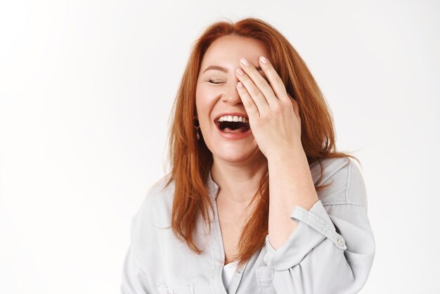 Felicidad envejecimiento concepto de belleza Despreocupada guapa pelirroja mujer de mediana edad riendo alegre tocar cara cerrar ojos risita emotivo divertirse círculo familiar disfrutar jubilación fondo blanco