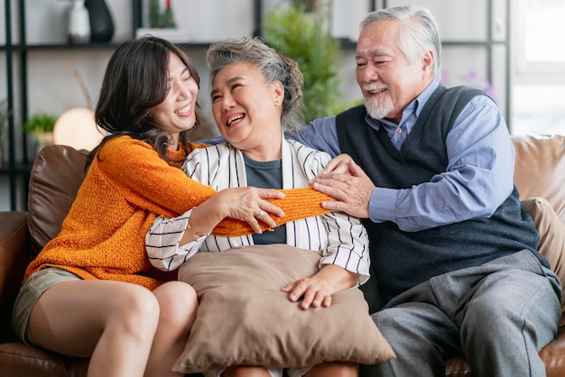 Felicidad familia asiática sincera de hija abrazo abuelo madre más anciano anciano acogedor relajarse en el sofá sofá sorpresa visitando en la sala de estar en casa juntos abrazar alegre familia asiática en casa