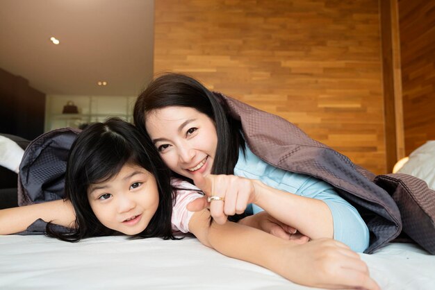 La felicidad de la madre y la hija juegan con la manta junto con el amor en el fondo interior del dormitorio de la cama