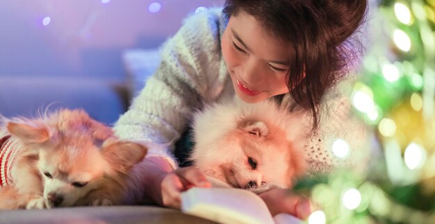 Felicidad navideña con suéter casual femenino asiático siéntate, relájate leyendo un libro novedoso con un perrito faldero, siéntate junto con almejas y alegre concepto de ideas festivas navideñas