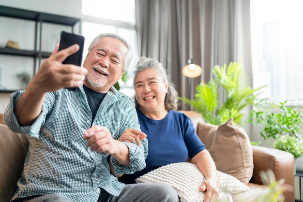 Felicidad, una pareja asiática de ancianos jubilados disfruta de una videollamada a la familia juntos en un sofá en la sala de estar en casa.