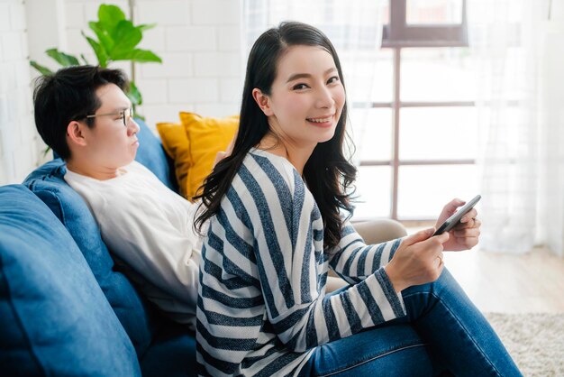 Felicidad pareja dulce asiática disfruta del juego en el teléfono inteligente juntos sala de estar fondo de casa