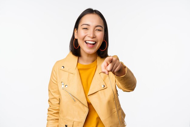 Felicidades eres tú Feliz hermosa mujer asiática riéndose señalando con el dedo a la cámara eligiendo invitar a la gente a reclutar de pie sobre fondo blanco