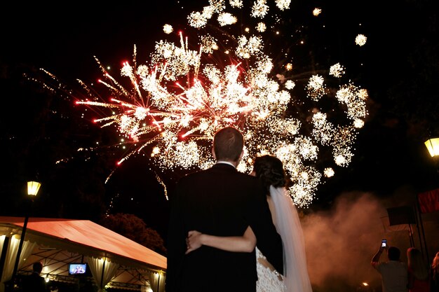 Feliz abrazos novia y el novio viendo hermoso colorido fuegos artificiales cielo nocturno