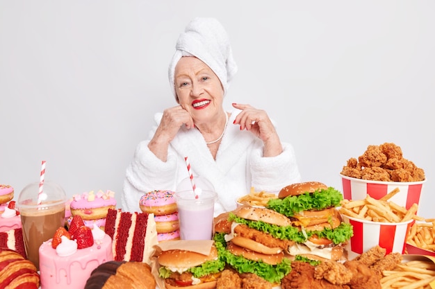 Feliz abuela disfruta del día de la comida trampa rodeada de comida chatarra