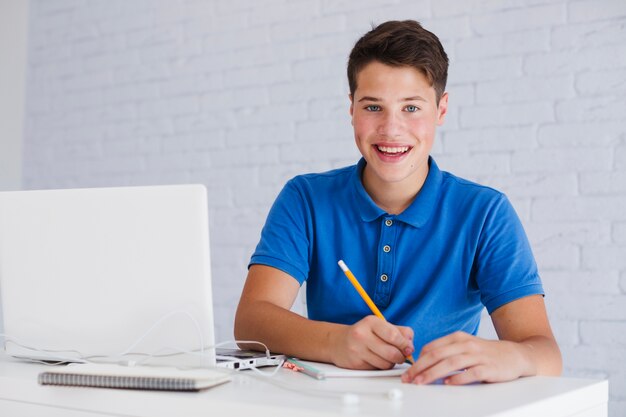 Feliz adolescente haciendo notas cerca de la computadora portátil