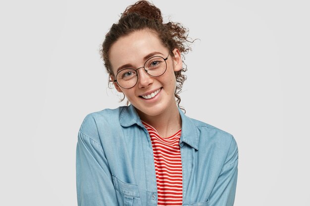 Feliz adolescente pecoso con gafas posando contra la pared blanca