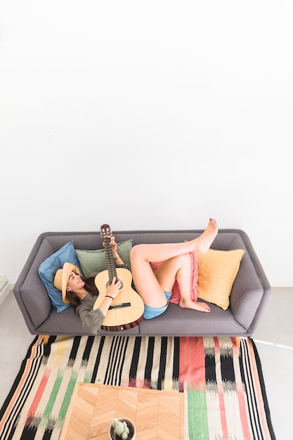 Foto gratuita feliz adolescente tumbado en el sofá tocando la guitarra