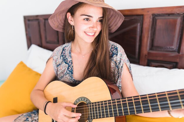 Feliz adolescente vistiendo sombrero tocando la guitarra