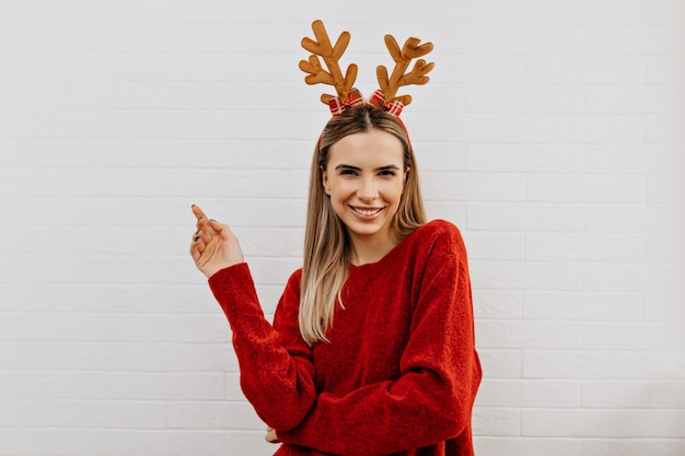 Feliz adorable dama en jersey rojo en sombrero de navidad sonriendo y mirando a la cámara sobre fondo aislado