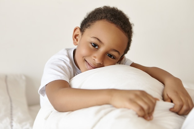 Feliz adorable niño de piel oscura de origen africano relajándose en la cama el fin de semana después de despertar