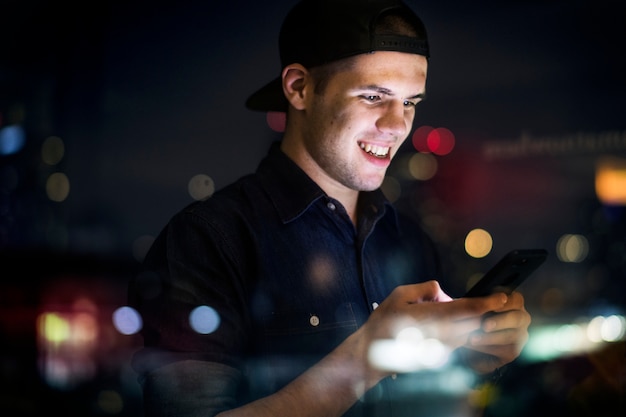 Feliz adulto joven macho usando un teléfono inteligente en un paisaje urbano de noche