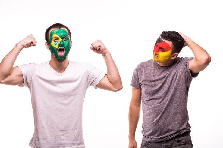 Foto gratuito feliz aficionado al fútbol de brasil celebrar la victoria sobre el aficionado al fútbol molesto de los equipos nacionales de alemania con la cara pintada aislado sobre fondo blanco.
