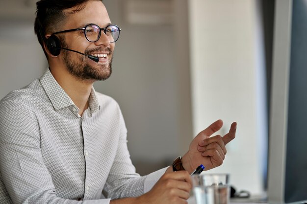 Feliz agente del centro de llamadas que usa la computadora mientras se comunica con los clientes y trabaja en la oficina