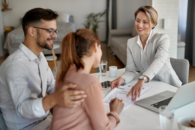 Feliz agente inmobiliario reuniéndose con una pareja joven y señalando el lugar de la firma de su contrato