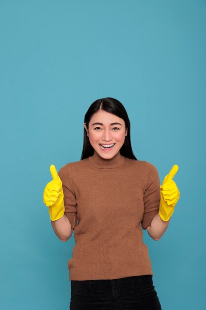 Feliz, alegre y alegre trabajadora doméstica asiática de las tareas domésticas con los pulgares hacia arriba usando guantes amarillos para la seguridad de las manos, trabajadora de ama de casa, concepto de limpieza del hogar, mujer sonriente satisfecha y optimista