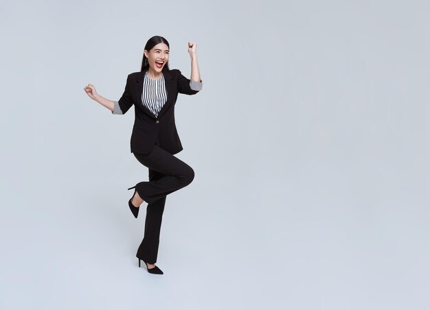 Feliz alegre joven empresaria asiática en traje saltando en el aire sobre fondo blanco de estudio