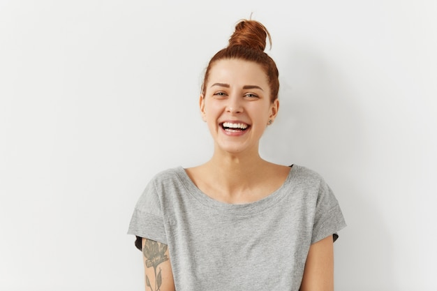 Foto gratuita feliz alegre joven vistiendo su pelo rojo en moño, mirando alegre y encantadora sonrisa