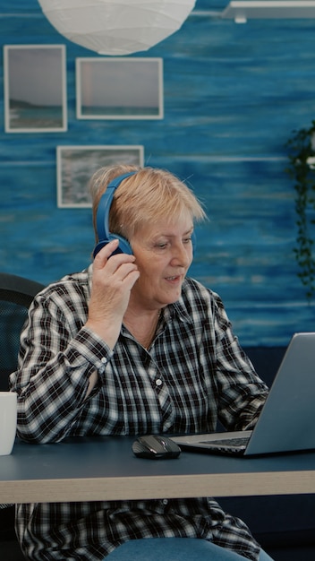 Feliz anciana con auriculares escuchando música mientras verifica las estadísticas