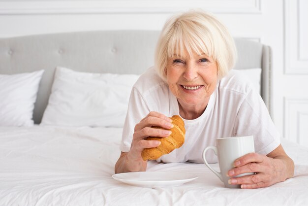 Feliz anciana sosteniendo una taza y un croissant