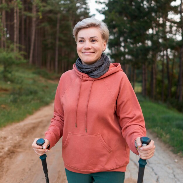 Feliz anciana turista en el bosque con bastones de senderismo