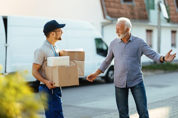 Feliz anciano dando la bienvenida al mensajero que le está entregando paquetes en casa