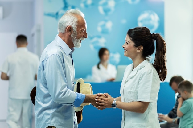 Feliz anciano estrechando la mano con una doctora mientras habla en el vestíbulo de la clínica