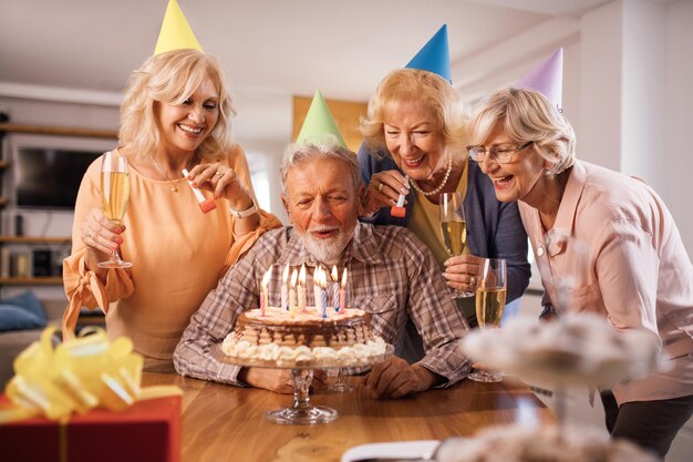 Feliz anciano soplando velas de cumpleaños mientras celebra con amigos en casa