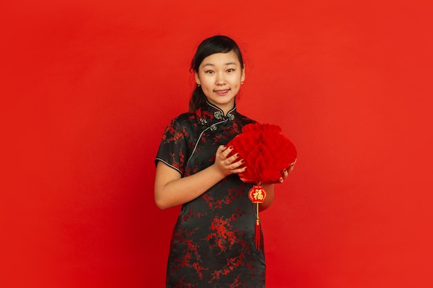 Feliz año nuevo chino 2020. Retrato de joven asiática aislado sobre fondo rojo. Modelo femenino en ropa tradicional se ve feliz y sonriente con decoración. Celebración, fiesta, emociones.