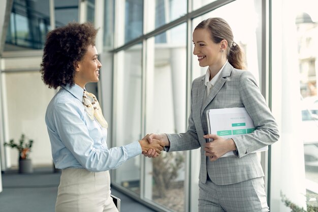 Feliz apretón de manos de mujeres empresarias mientras saludan en un pasillo