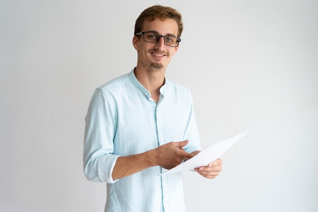 Feliz apuesto joven en gafas trabajando con papel y mirando a cámara.