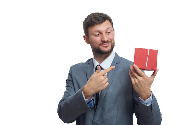 feliz apuesto joven en un traje sonriendo apuntando a la caja de regalo