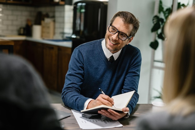 Feliz asesor financiero comunicándose con una pareja y tomando notas en su cuaderno