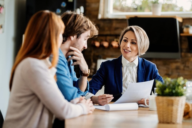 Feliz asesor financiero y una pareja joven comunicándose mientras revisan el papeleo durante una reunión