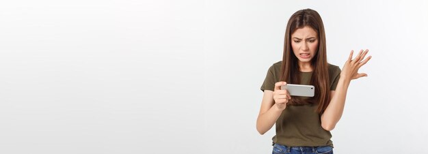 Feliz y atractiva chica morena disfrutando de ganar en un videojuego en un smartphone aislado sobre un fondo gris