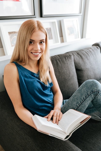 Feliz atractivo joven womna leyendo el libro en casa