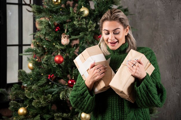 Feliz bastante joven sosteniendo una caja de regalo cerca de un árbol de Navidad