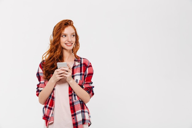 Feliz bella joven pelirroja dama chateando por teléfono móvil.