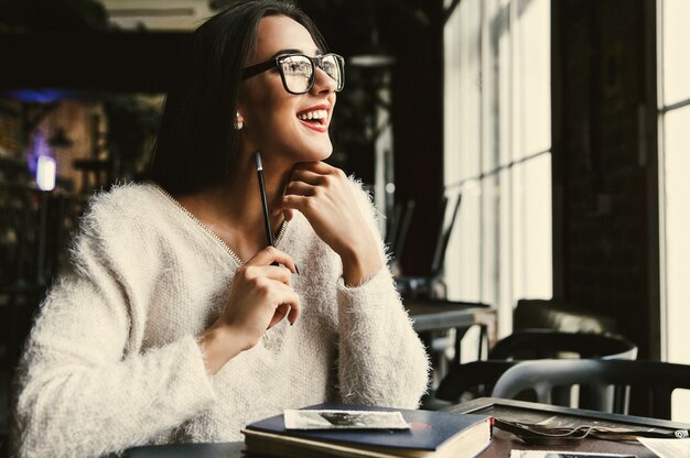 Feliz bella mujer hace algunas notas sentado en el café