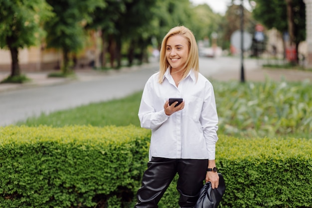 Feliz bella mujer joven usando su teléfono inteligente caminando por la calle de la ciudad