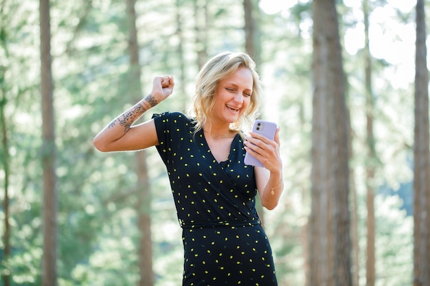La feliz bloguera está levantando el puño hablando por videollamada sobre el fondo de la naturaleza