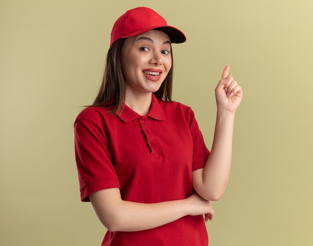 Feliz bonita mujer de entrega en uniforme apunta hacia arriba