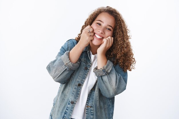 Feliz carismática tierna tonta gordita linda chica tocando las mejillas sonriendo alegremente tener el mejor día disfrutar de la vida divirtiéndose haciendo un buen pie chaqueta de mezclilla de pared blanca tonto imitando