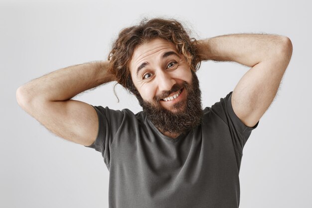 Feliz carismático hombre del Medio Oriente con barba, sonriendo y peinándose