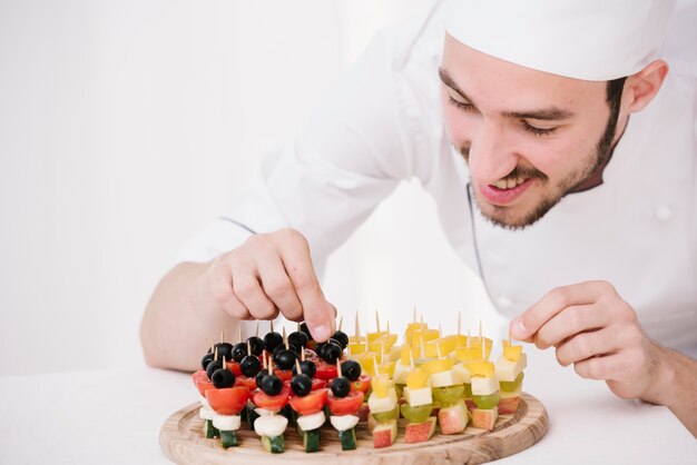 Feliz chef arreglando bocadillos en tablero de madera