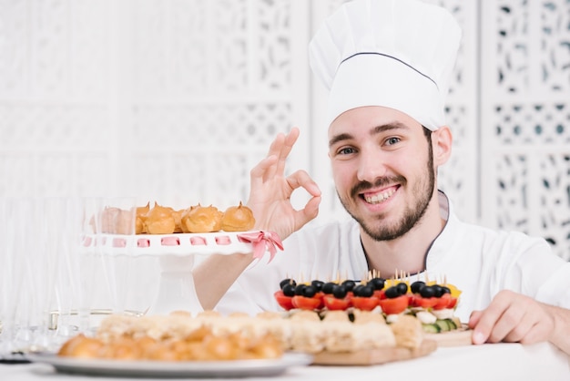 Feliz chef presentando comida en una mesa