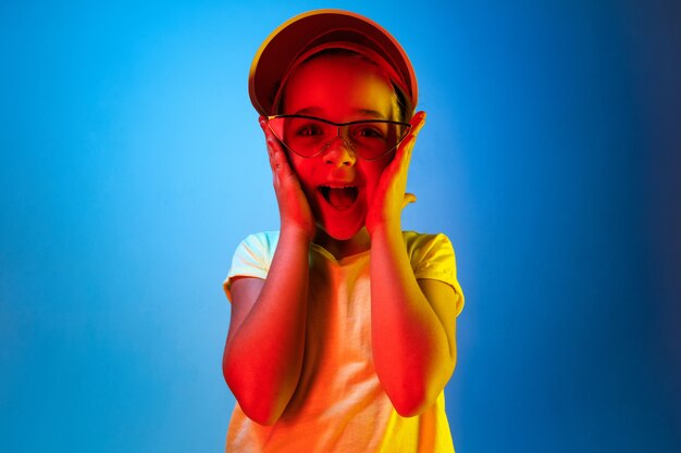 Feliz chica adolescente de pie y sonriendo aislado en el espacio de neón azul de moda. Hermoso retrato femenino. Joven, satisfacer, niña